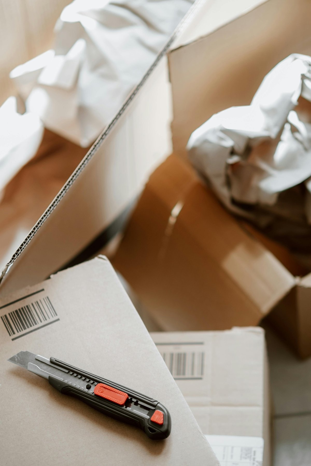Box cutter knife on opened cardboard boxes with packing materials and bubble wrap